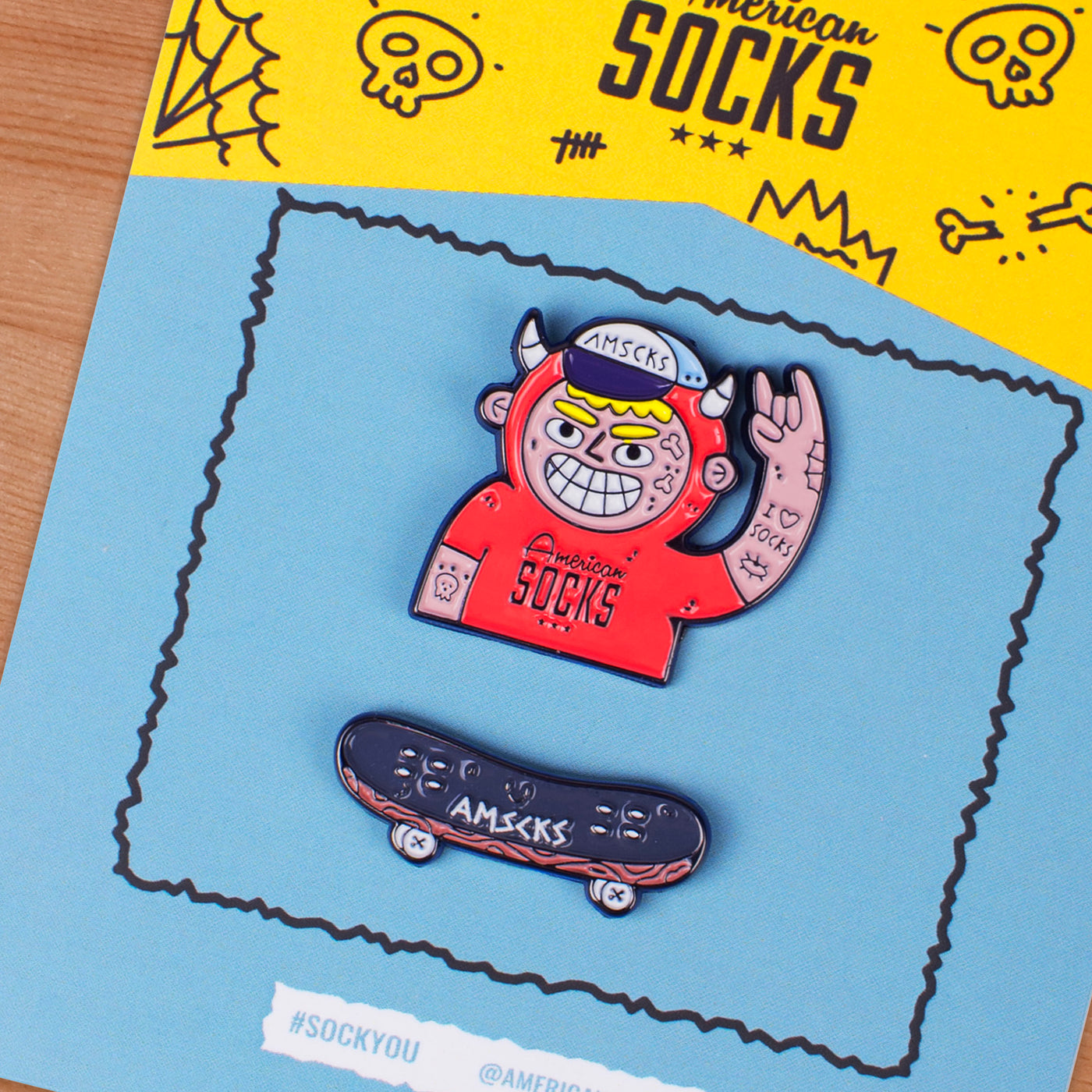 Close up of cool pin pack containing fun punk character making the rock hand sign pin and a skateboard pin american socks