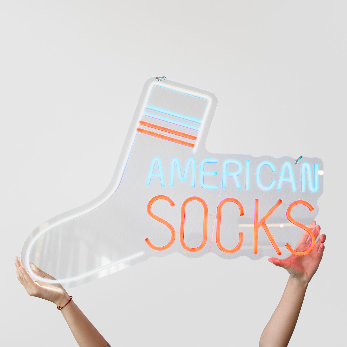 Hands holding a sock shaped neon sign that reads american socks on a white background