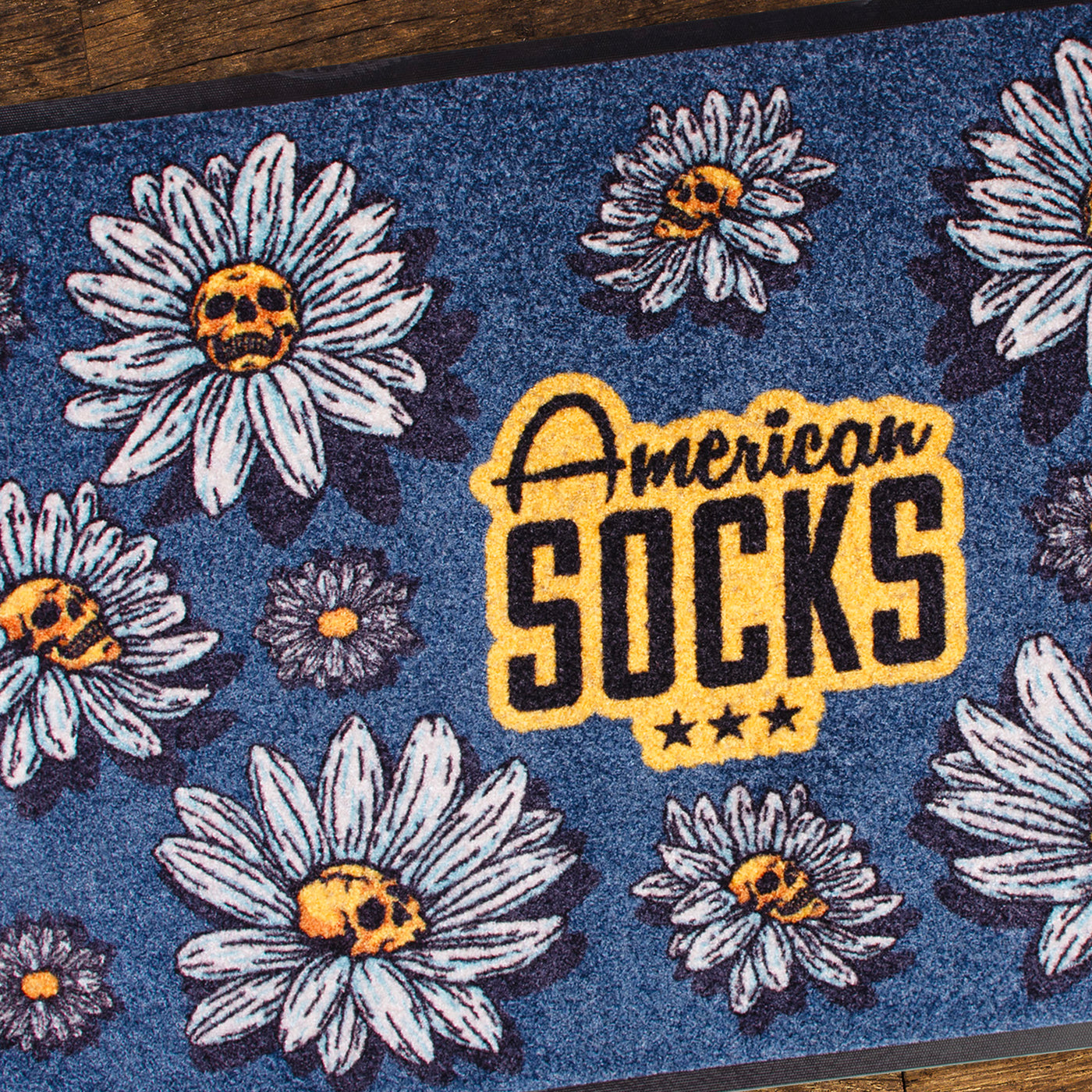 Close up of floral patterned rug with punk daisy flowers with skulls in the middle design and american socks logo in the center 