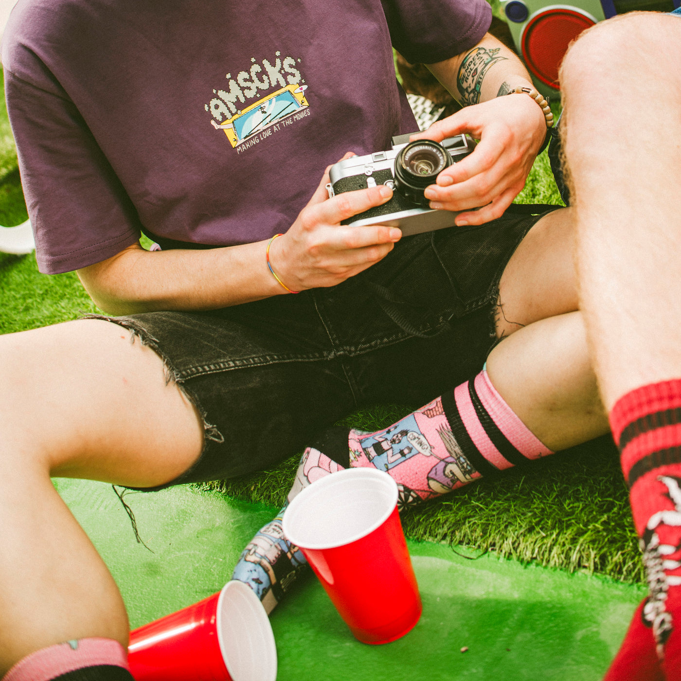Person sitting on the ground wearing skater clothes and funky socks while holding a camera american socks